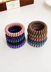 Gros plan d'élastiques à cheveux spirales mats aux couleurs Morandi sur un bureau blanc