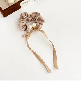 Detail of champagne satin scrunchie with rhinestones, pearls, and ribbon bow accent