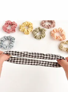 Detail showing elastic black and white gingham scrunchie being stretched by hands