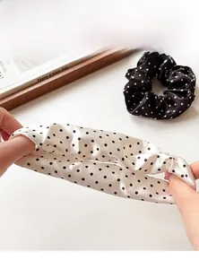 Close-up of elastic polka dot satin scrunchies being stretched for durability detail