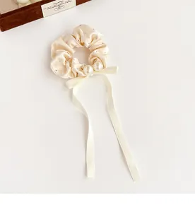 Detailed view of cream satin hair scrunchie with rhinestones, pearls and bow ribbons