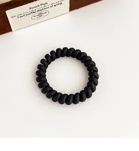 Gros plan sur un chouchou spirale noir mat sur un fond crème minimaliste avec accessoires