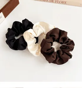 Drei Satin-Haargummis in Schwarz, Creme und Braun auf minimalistischem Hintergrund