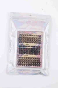 Macro view of fluffy black individual lash clusters in clear tray with holographic bag