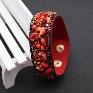 Detail of red leather cuff bracelet featuring crushed stones and gold pyramid studs