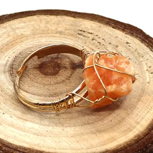 Detalle macro de piedra natural naranja envuelta en hilo dorado sobre madera