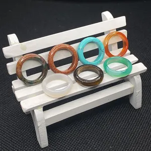 Macro view of seven assorted colorful natural stone rings on a white miniature bench display