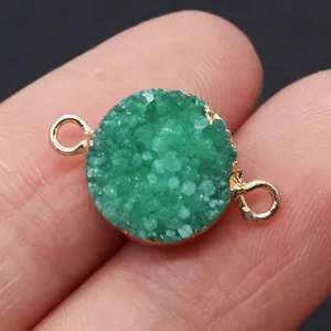 Macro view of a round dark green druzy stone connector with gold plating held by fingers