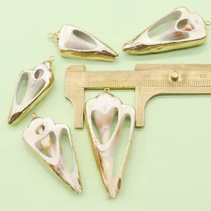 Macro detail of natural shell pendants with gold plated edges next to a brass caliper