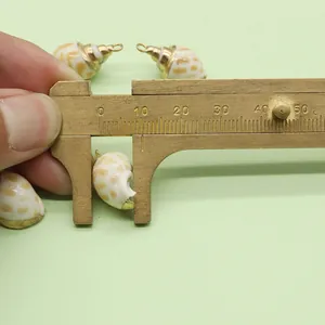 Schuifmaat meet een natuurlijke schelphanger met vergulde randen voor DIY sieraden
