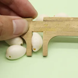 Macro view of measuring a 15mm natural cowrie shell bead with brass calipers for DIY jewelry