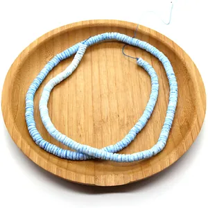 Detail of light blue disc shell beads on a string inside a wooden tray for DIY jewelry