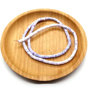 Detailed close-up of purple and white disk-shaped Heishi beads on a wooden tray