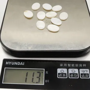 Polished white oval natural shell beads weighing approximately 11 grams on a digital scale