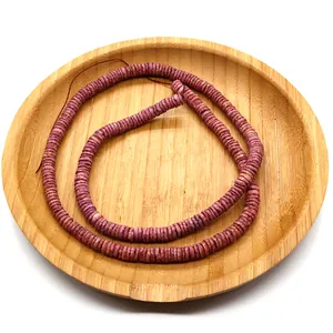 Flat pink purple heishi shell beads arranged in a spiral on a natural bamboo tray