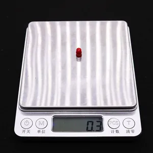 Macro shot showing 0.3g weight of red gourd-shaped synthetic coral bead on a digital scale