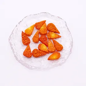 Carved orange synthetic coral drop beads with sunflower motifs on a glass plate