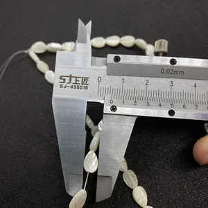 Macro shot showing measurement of a 12.5mm leaf-shaped white shell bead with leaf veins