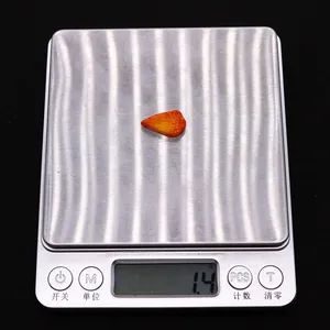 Close-up of a 1.4g carved orange coral drop bead with leaf texture on a digital scale