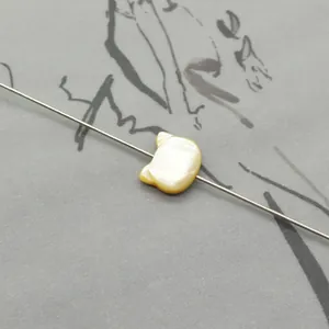 Macro view of a cat-shaped natural shell bead with iridescent luster on a display needle