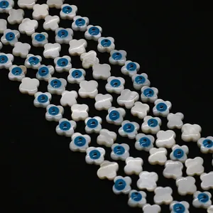 Détail macro de perles trèfles en nacre blanche avec motifs œil bleu sur fond noir profond