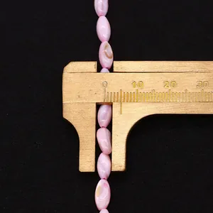 Macro-opname van roze rijstvormige schelpkralen met schuifmaat voor DIY-sieraden
