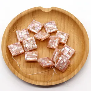Close-up of pink mosaic shell square beads with iridescent luster on a wooden tray