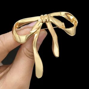 Close-up of elegant gold bow brooch held in hand showing mirror-polished finish