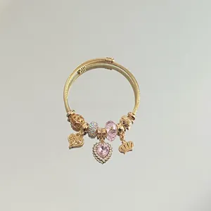 Detail of gold woven bracelet with pink heart charms and a crown pendant