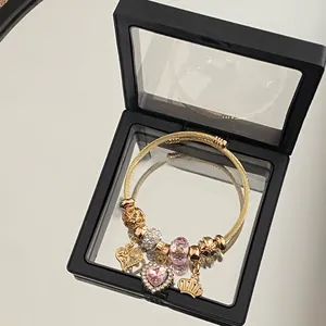 Detail of gold charm bracelet with pink heart and crown in a black jewelry box