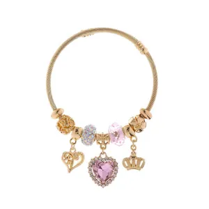 Golden spiral wire bracelet featuring pink heart crystal pendant and crown charms