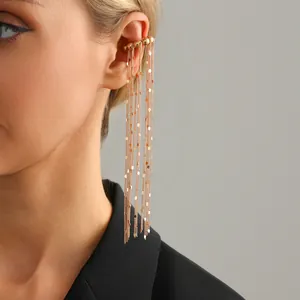 Macro detail of a minimalist gold tassel ear cuff featuring long delicate chains