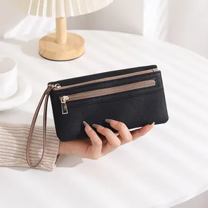 Detail of black pebbled leather wallet with double zippers and wristlet on white table