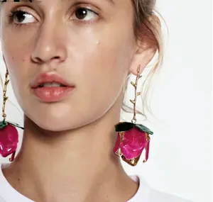 Detail of a pink enamel rose earring with gold branch stem shown on model