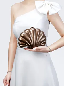 Close-up of a bronze shell-shaped metallic clutch bag held by a model in a white gown