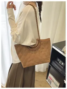 Detail of a brown quilted suede tote bag with bronze chain strap and round metal handle