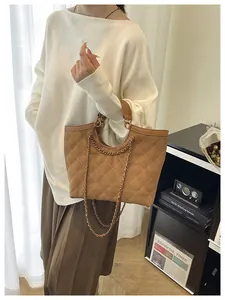 Close-up of brown quilted tote bag with chain strap held by model in casual outfit