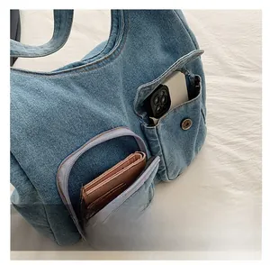 Détail du sac à bandoulière en denim avec poche zippée avant et compartiment à bouton