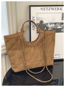 Detail of brown quilted suede tote bag featuring chain straps on a reflective surface