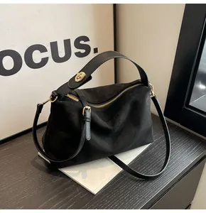 Détail d'un sac cabas en suède noir mat avec fermoir rotatif doré et anses en cuir