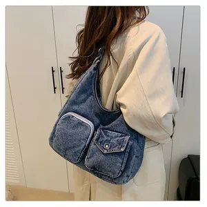 Détail du sac hobo en denim bleu avec poches frontales porté sur un trench-coat beige