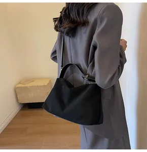 Détail du sac hobo en daim noir mat avec double bandoulière porté sur un blazer gris