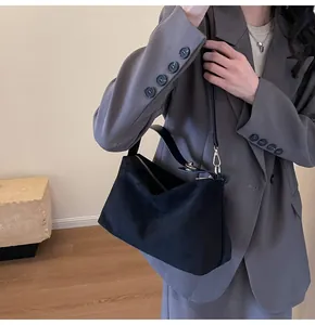 Détail du sac Boston noir mat avec ferrures dorées porté sur un blazer gris