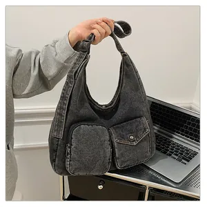 Détail du sac hobo en denim noir avec une poche zippée et un rabat à bouton-pression en métal