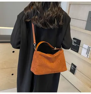Sac Boston en daim caramel porté avec un manteau noir dans un décor de bibliothèque