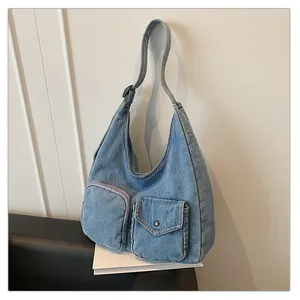 Détail du sac en jean montrant la large bandoulière et les poches plaquées à l'avant