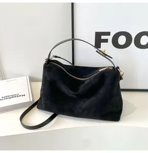 Détail d'un sac Boston en daim noir avec fermeture éclair dorée et bandoulière réglable