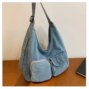 Détail du sac en denim bleu clair avec deux poches frontales et large bandoulière réglable