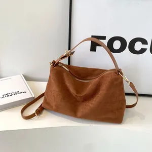 Détails du sac boston en daim caramel montrant la texture mate et les boucles dorées