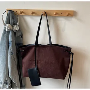 Détail macro du sac cabas en daim marron avec texte TOTE BAG embossé et pendentif